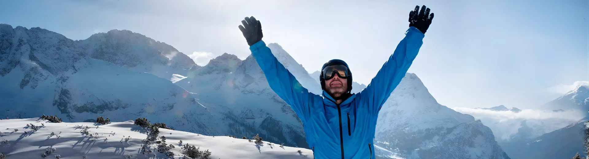Skiër juicht met opgeheven armen op een besneeuwde bergtop