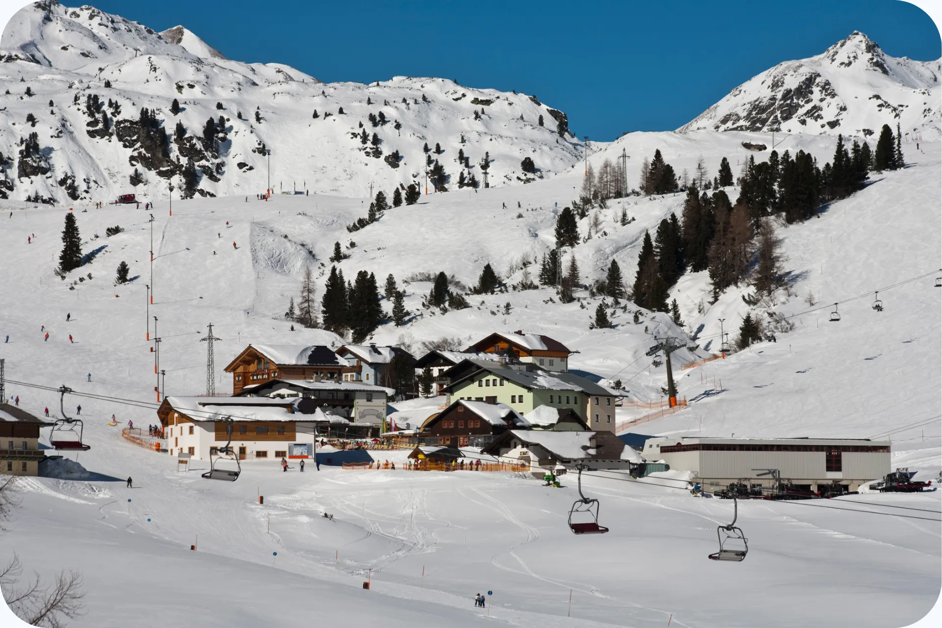 Besneeuwde skipistes in Obertauern met skiliften, chalets en bergtoppen onder een heldere blauwe lucht.