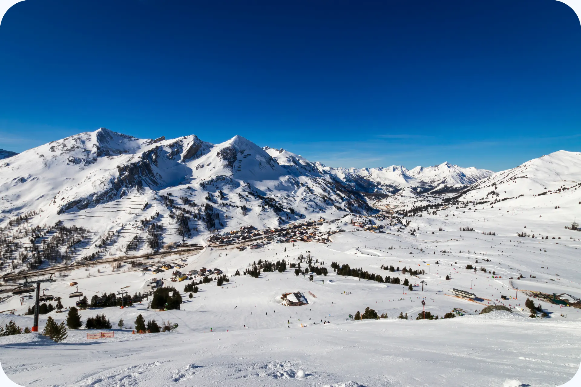 Panoramisch uitzicht over het besneeuwde skigebied van Obertauern met brede pistes, bergtoppen en het dorp in het dal.
