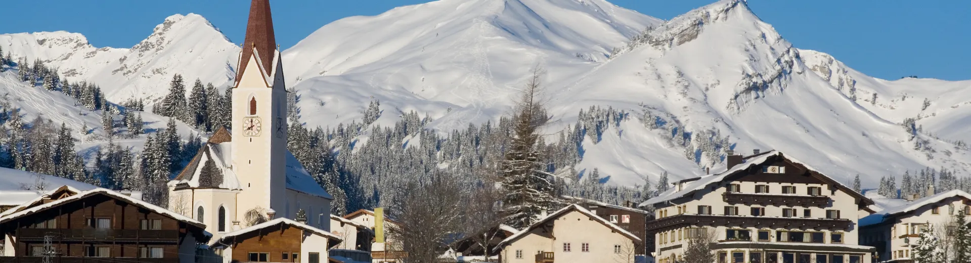Besneeuwd bergdorp Berwang in de Tiroler Zugspitz Arena met kerk, chalets en skipistes op de achtergrond.