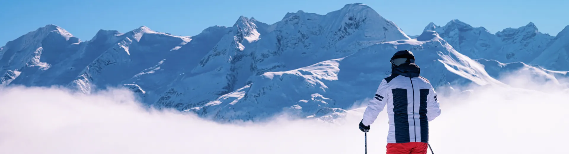Een skiër die uitkijkt over de bergen in het Zillertal Arena met wolken voor zich uit.
