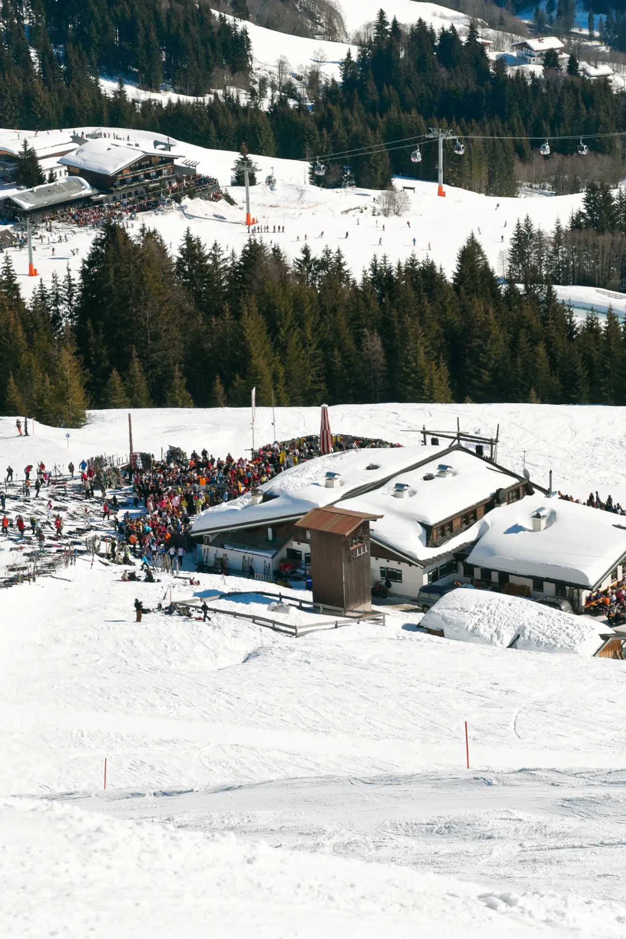 Op de voorgrond en de achtergrond een Après ski hut die beide drukbezocht zijn.