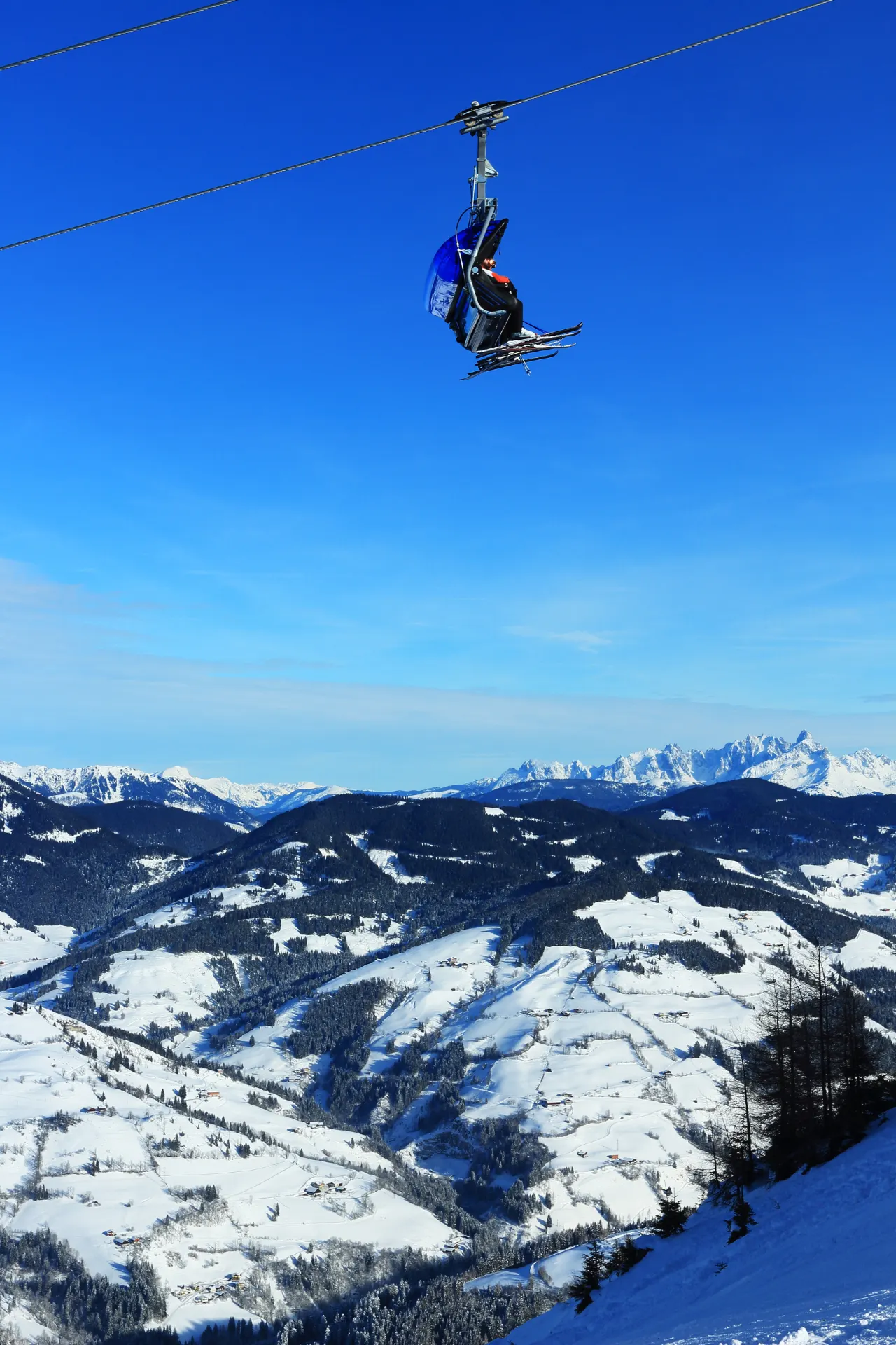 Een skilift hoog in de lucht met op de achtergrond uitzicht over de bergen.