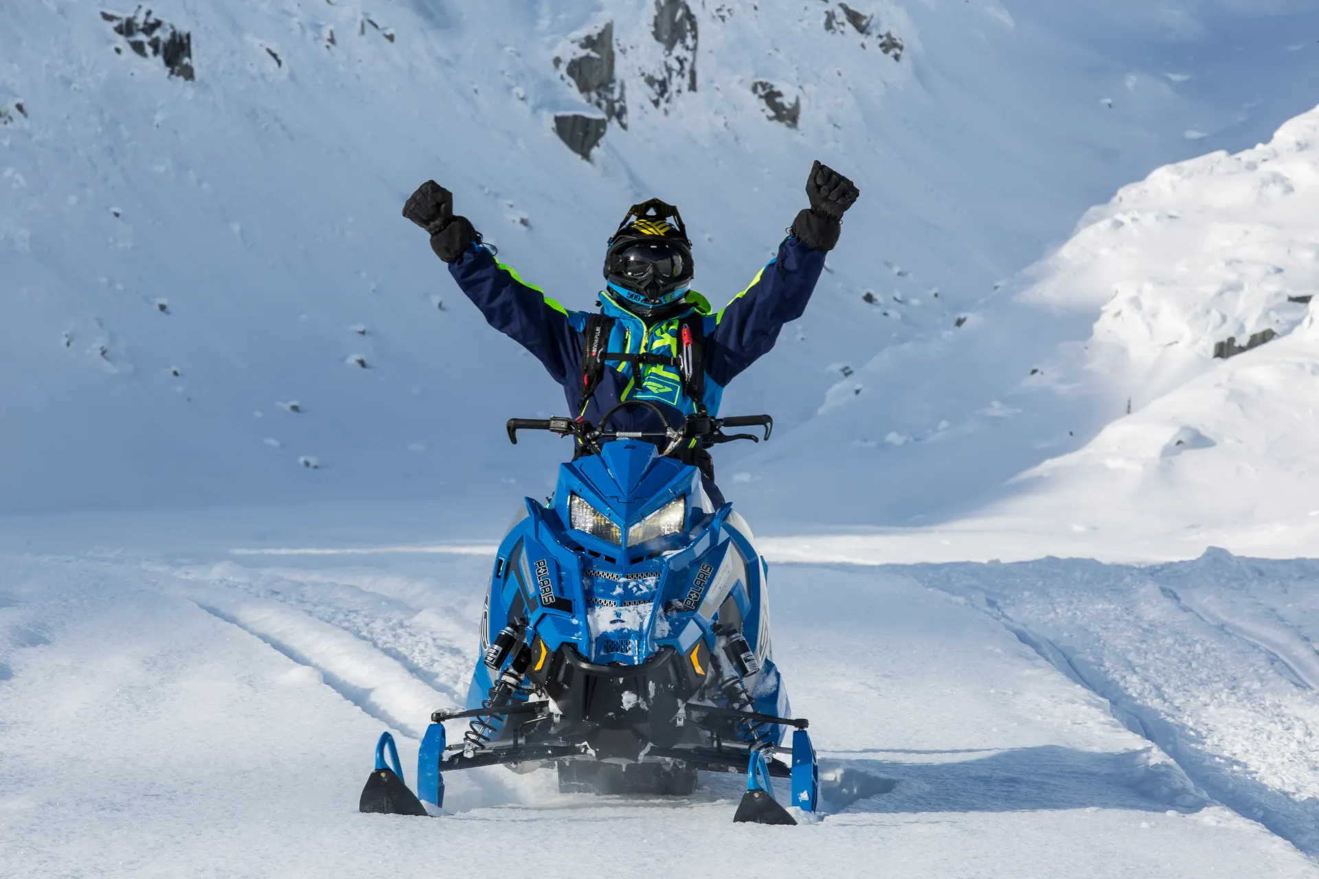 Man met helm op een sneeuwscooter met de handen omhoog.